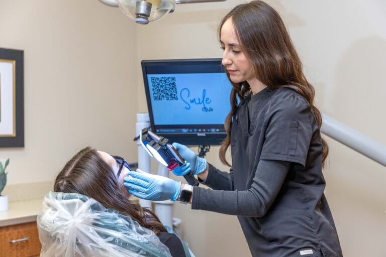 Dentist holding dental equipment while examining female patient in dental chair for gum bleaching